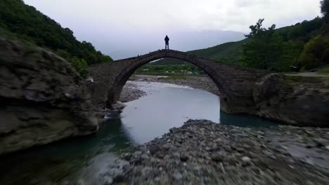 Man-stands-on-a-narrow-bridge-under-which-water-flows