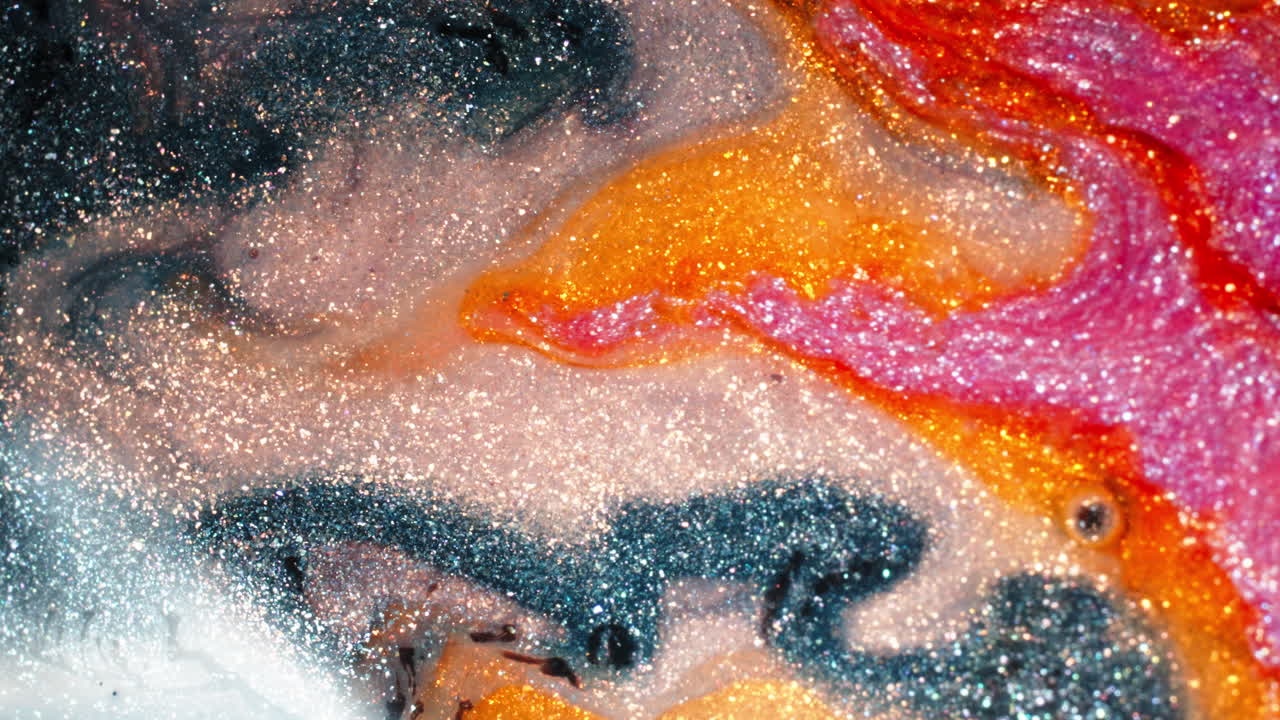 Shimmering pigments of orange blue and white swirl and blend in a mesmerizing abstract pattern