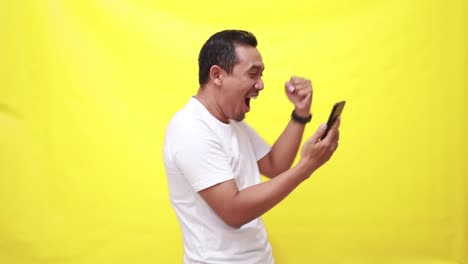 Smartphone,-excited-with-asian-man-isolated-yellow-background-in-studio,-celebration-and-social-media-giveaway