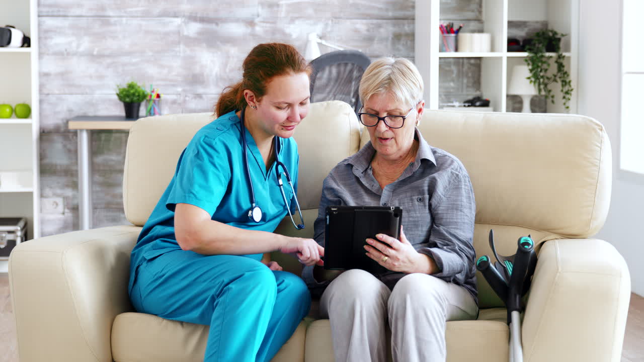 Female nuse helping senior elderly retired woman how to use her tablet computer