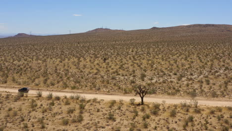 Large-black-SUV-drives-quickly-down-a-dirt-road-in-the-Mojave-Desert-and-passes-two-other-dirt-roads