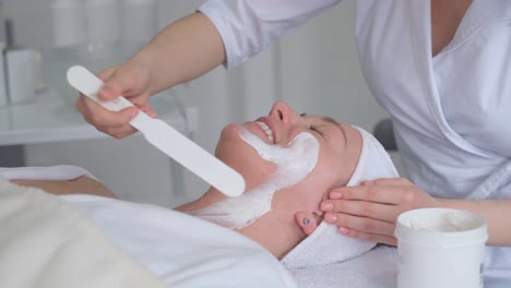 a cosmetologist is seen in close-up, applying moisturizer to the lips of a young woman after a permanent makeup procedure. a modern beauty salon, and the view is from above.