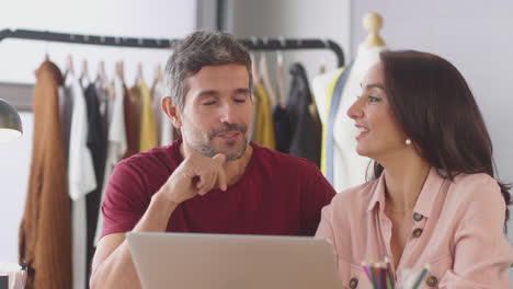 diseñadores de moda masculinos y femeninos en el estudio teniendo una discusión en el escritorio con una computadora portátil