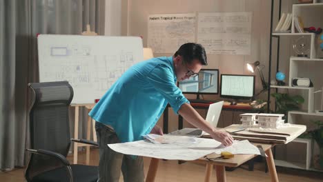 asian man engineer with a laptop looking at blueprint while working at the office