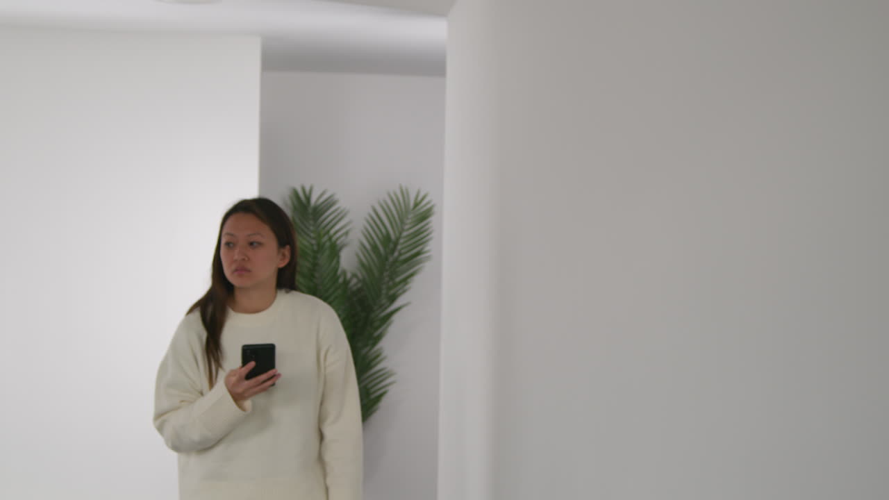 mujer estresada o ansiosa sentada en el suelo apoyada en la pared en casa reaccionando a un mensaje de noticias o historia en internet o redes sociales en el teléfono móvil 3