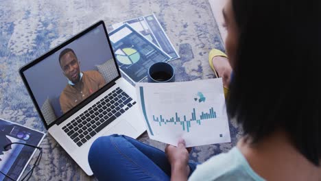African american woman holding a document having a video call with male colleague on laptop