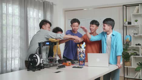 3d 프린팅을 가진 젊은 아시아 소년 그룹이 집에서 노트북에서 사이보그 손을 작업하는 동안 함께 손을 잡고 있습니다.