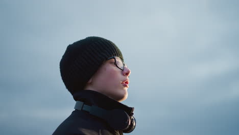 side view of a young boy in a black outfit and glasses lifting a ball with a headset around his neck, with his mouth slightly open