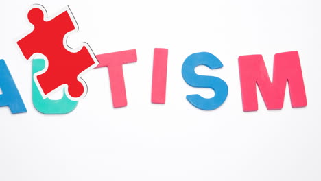 animación de piezas de rompecabezas rojas y amarillas que caen sobre texto de autismo sobre fondo blanco