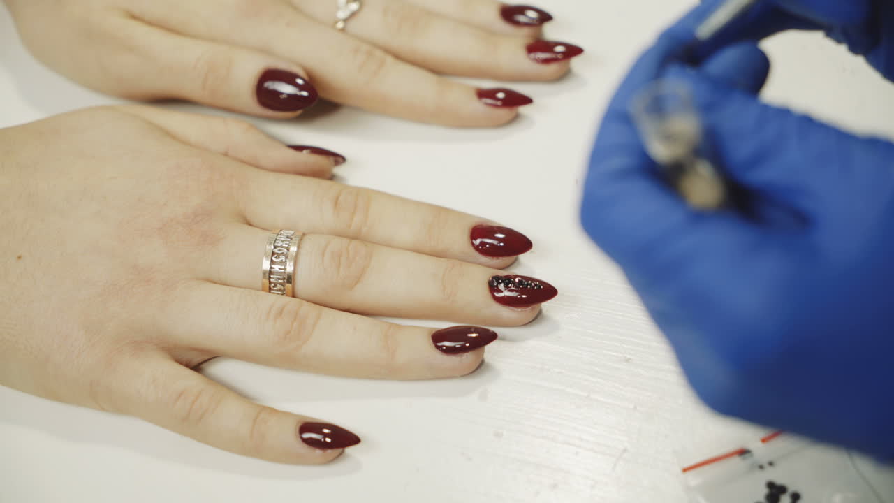 Manicurist applying red nail varnish. Rhinestones on nails