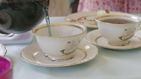 Tea-pouring-into-fine-china-cups-with-a-hint-of-vintage-charm,-close-up