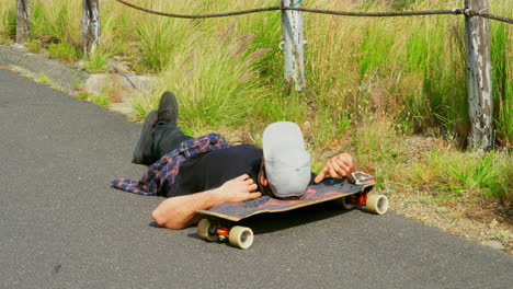 Modern young male skateboarder lying on the road with his head on a skateboard at countryside 4k