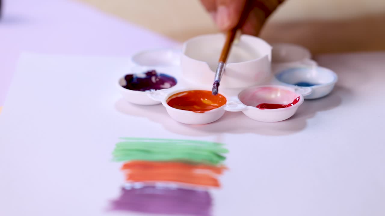 Artist hand dips brush in palette, vibrant watercolor strokes on paper, soft natural lighting