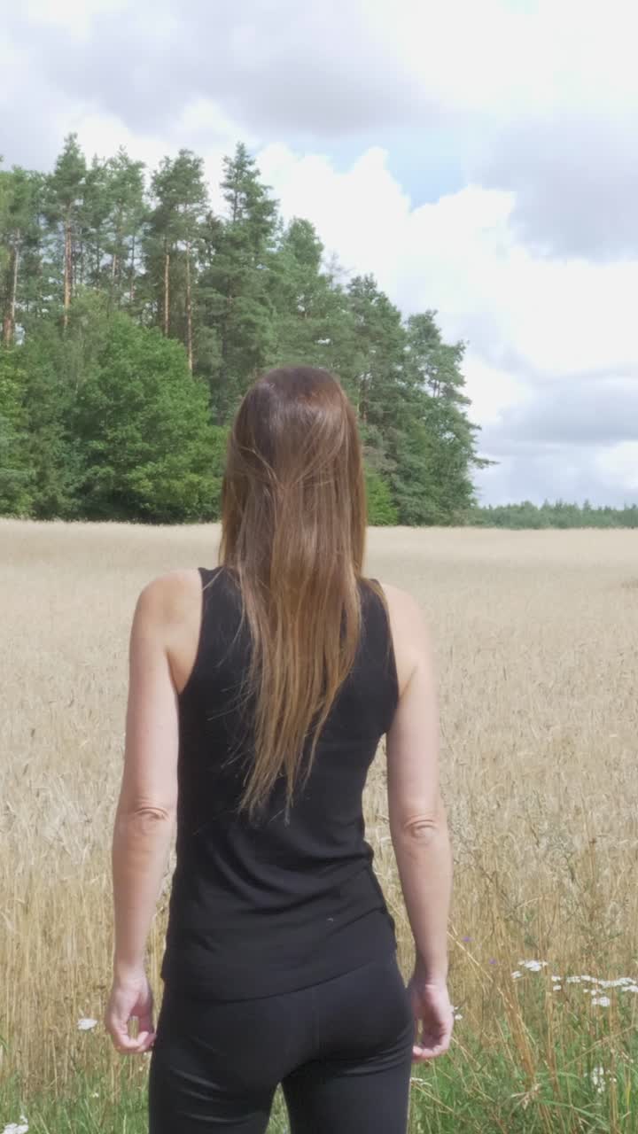 Woman from behind looking at a beautiful wheat field and forest on a sunny summer day