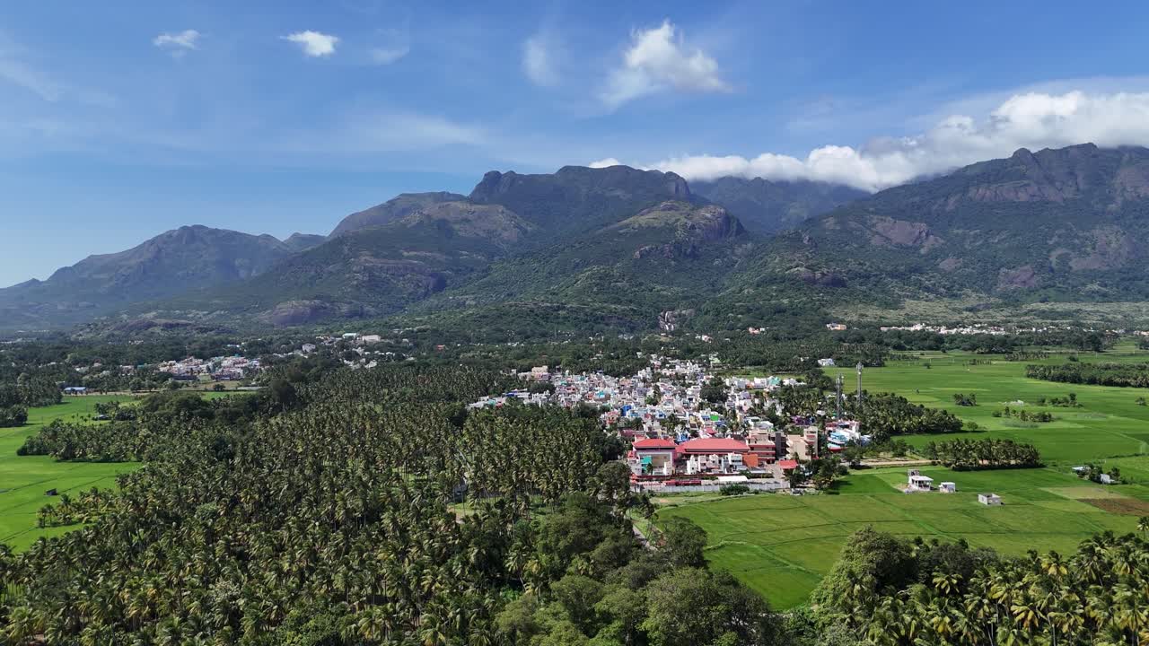 High-angle drone footage of a scenic view of a colourful town at the base of lush mountains in South India. Ideal for travel, culture, and nature themes