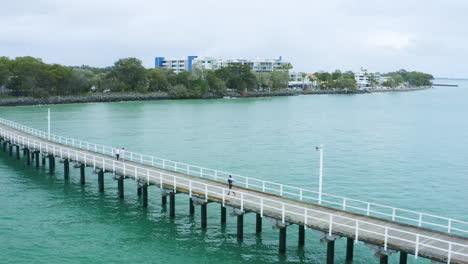 Sportlerläufer-Auf-Langem-Pier-über-Der-Wasserpromenade,-4k-Drohnenüberführung-Aus-Der-Luft