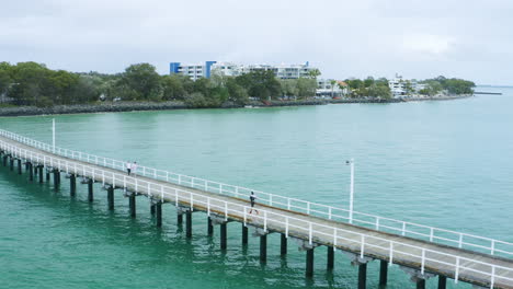 corredor de atletas en el muelle del paseo marítimo largo sobre el agua, sobrevuelo aéreo de drones 4k