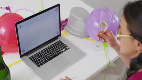 Happy asian woman with champagne making new year&#039;s eve video call on laptop with copy space