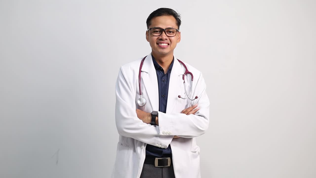 Dokter pria Asia yang menarik dengan tangan disilangkan, percaya diri, senyum ramah, suasana hati yang baik, mengenakan jas putih, terisolasi di latar belakang putih