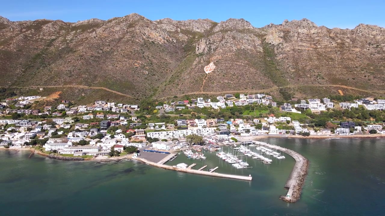 Porto e marina per yacht della città costiera di Gordon's Bay ai piedi delle montagne. Aerea.