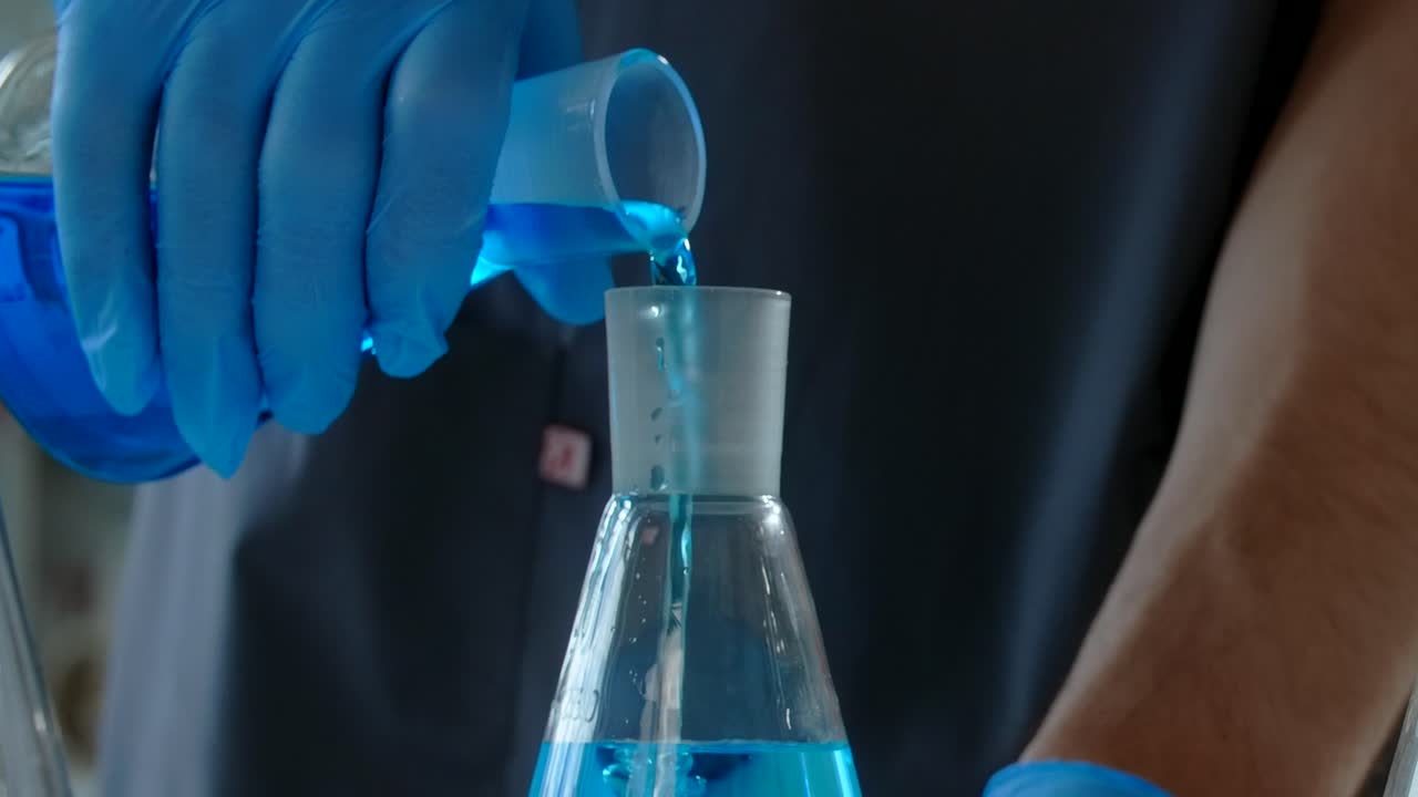 Scientist pouring a blue liquid into a flask
