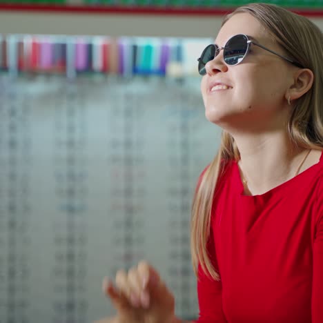 young woman trying on stylish sunglasses. pretty girl in red blouse dresses black eyeglasses indoors. eyesight concept.