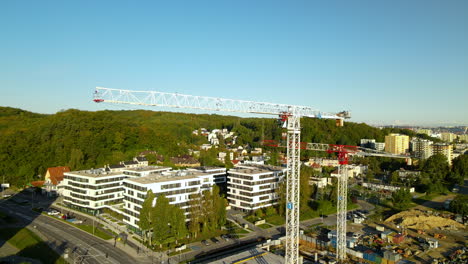 Flat-Top-Tower-Cranes-Erected-In-Gdynia,-Poland---Jib-Rotating-At-The-Construction-Site---pullback-drone-shot