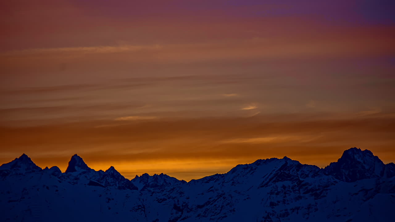Ripresa in time-lapse di nubi cirrostrato che volano su una catena montuosa innevata durante un tramonto epico all'orizzonte