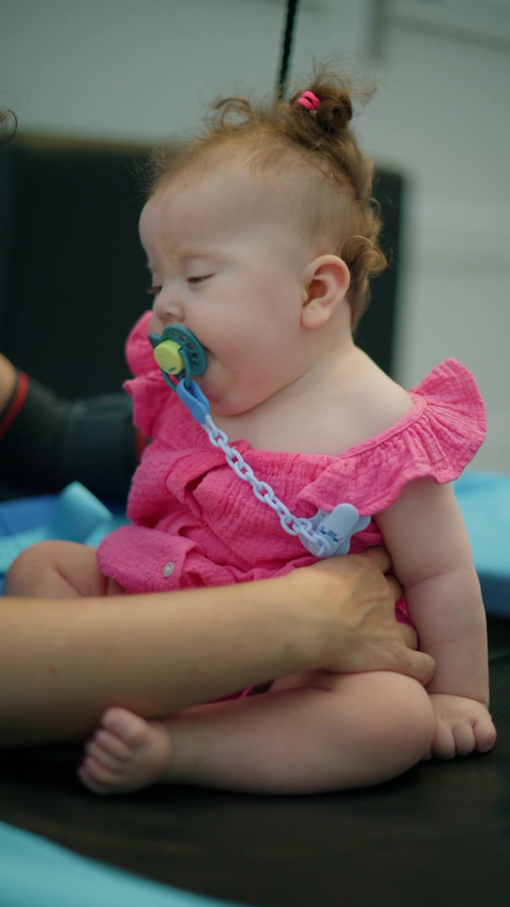 Mother's hands gently holding a baby girl wearing a pink dress and pacifier, providing comfort and care