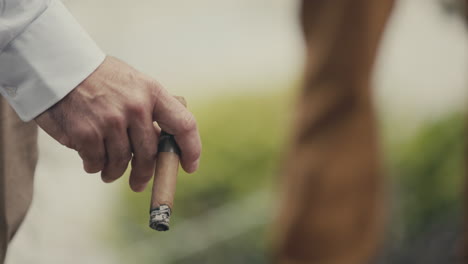 Male-Hand-Holding-Burning-Cigar-Against-Blurry-Backdrop