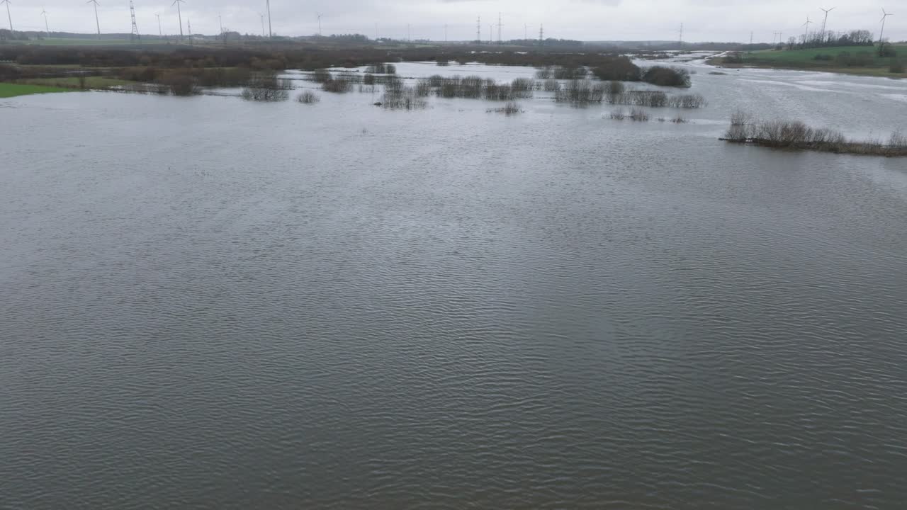 Aerial establishing view of high water in springtime, Alande river flood, brown and muddy water, agricultural fields under the water, overcast day, wide drone shot moving backward low