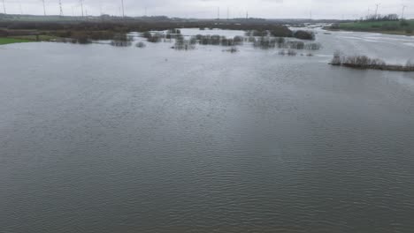 Aerial-establishing-view-of-high-water-in-springtime,-Alande-river-flood,-brown-and-muddy-water,-agricultural-fields-under-the-water,-overcast-day,-wide-drone-shot-moving-backward-low