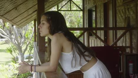 Young woman in white looking out from a tropical cabin, daydreaming, serene atmosphere, partial view