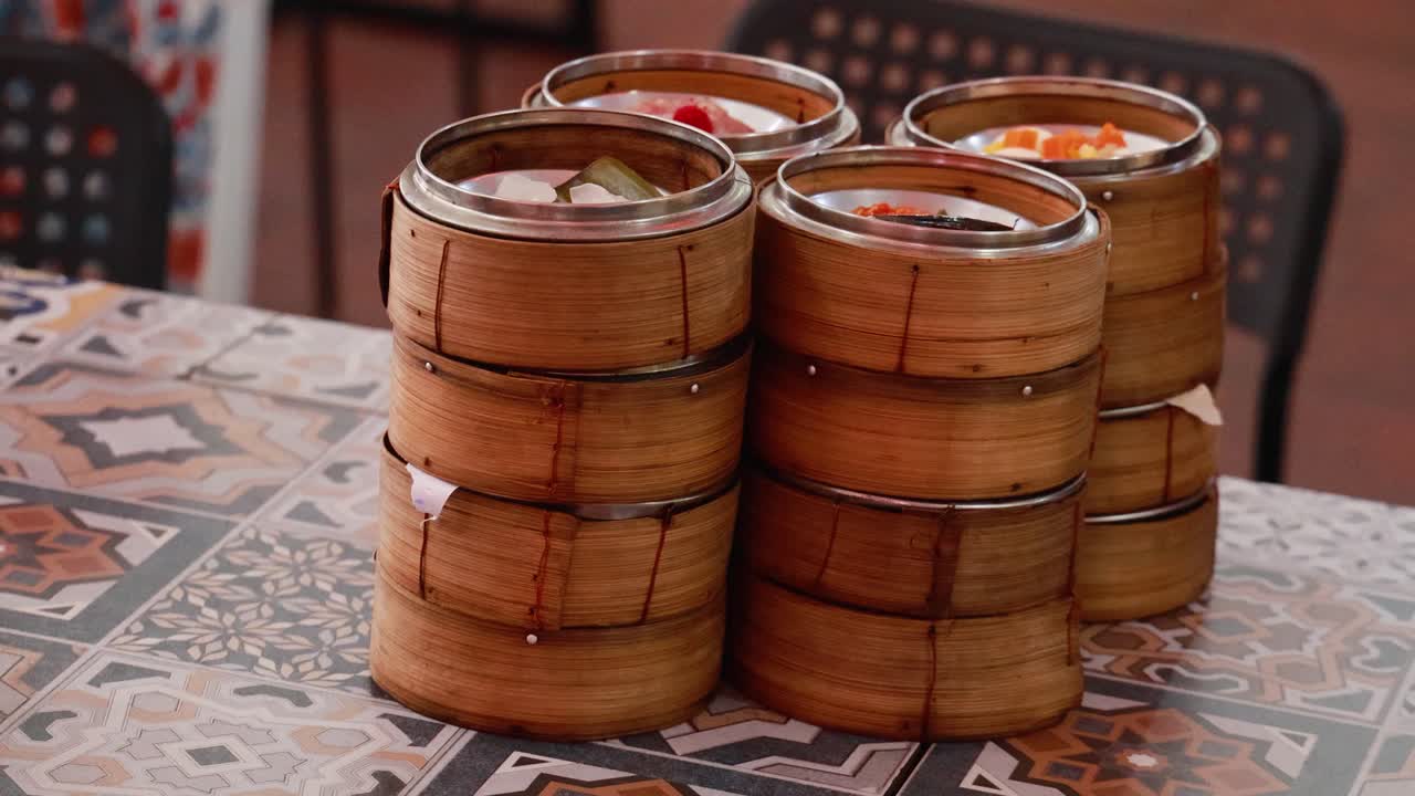 Hands arrange bamboo steamers filled with dim sum on a patterned table in a Phuket restaurant
