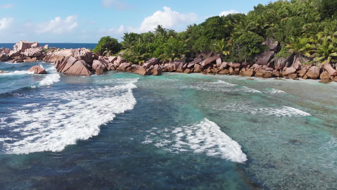 vista aérea siguiendo las olas rodando hacia las playas blancas y despobladas de anse coco, petit anse y grand anse en la digue, una isla de las seychelles