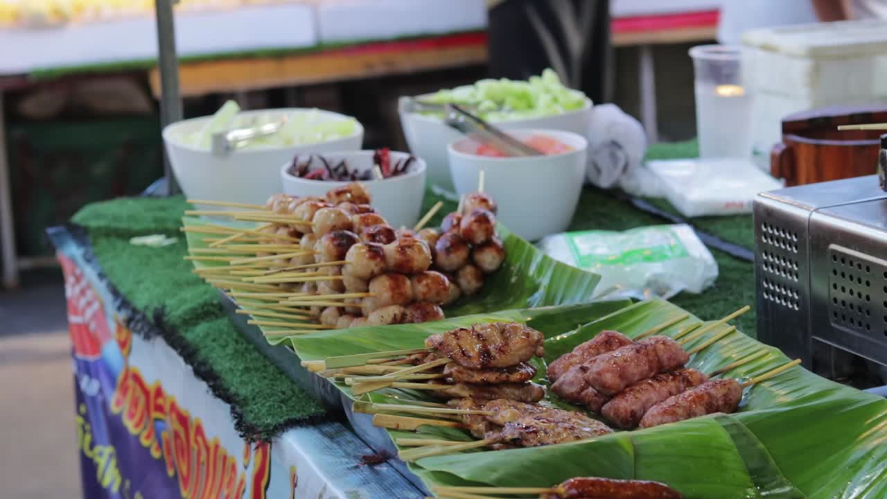 Bidikan Close-up Daging Babi, Sate Bakso, dan Daging Panggang Lainnya di Pasar Jalanan Lokal dengan Pelanggan yang Berjalan