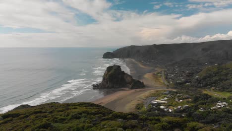 Vista-Aérea-Que-Revela-La-Roca-Del-León-En-La-Playa-De-Piha-De-Arena-Negra,-Nueva-Zelanda