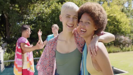 Portrait-of-happy-diverse-group-of-friends-embracing-and-holding-towels-in-summer