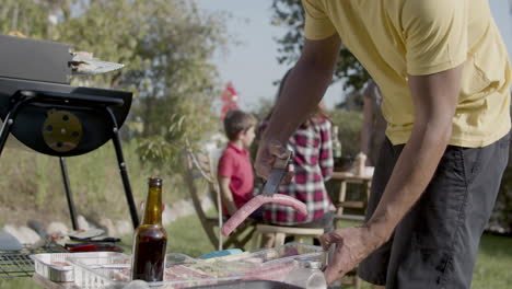 man taking raw kebab with tongs and putting it on barbecue grill