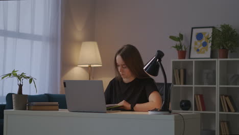 mujer está escribiendo la tarea en el cuaderno leyendo información de la pantalla de la computadora portátil tecnología moderna para la educación aprendizaje electrónico desde casa
