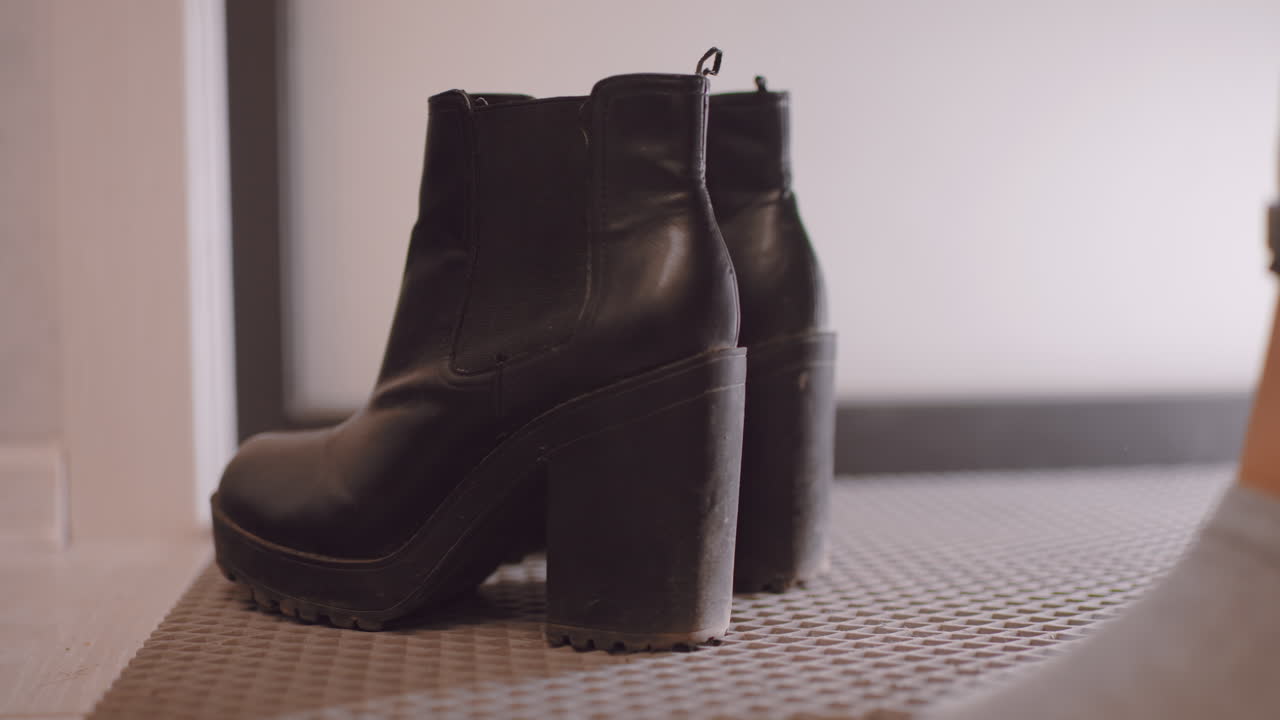 Close up of female hand reaching for black leather high heel boot to pull it off after wearing, showing detail of footwear, gesture, and everyday action of removing shoes at home entrance