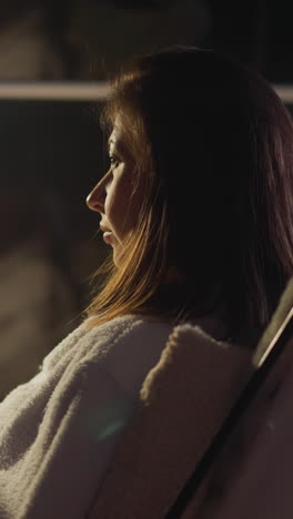 woman sits in armchair with cup of hot beverage in room lit by light of lantern. sad lady rests alone thinking about life problems. concept of depressed emotions