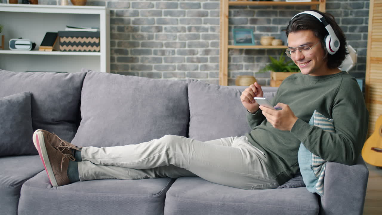 헤드폰과 전화로 소파에서 휴식을 취하는 남자