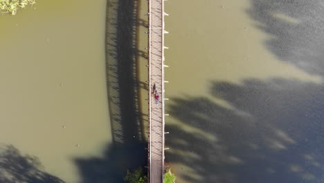 Vista-Aérea-Directamente-Sobre-Dos-Personas-Tendidas-En-Un-Puente-Peatonal-Sobre-El-Lago-Esmeralda-En-Melbourne,-Australia