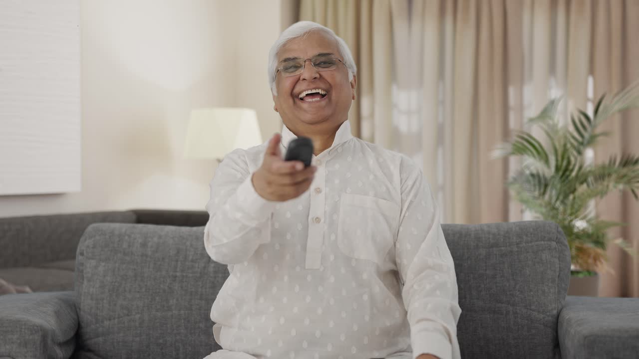 Glad ældre indisk mand ser tv og griner