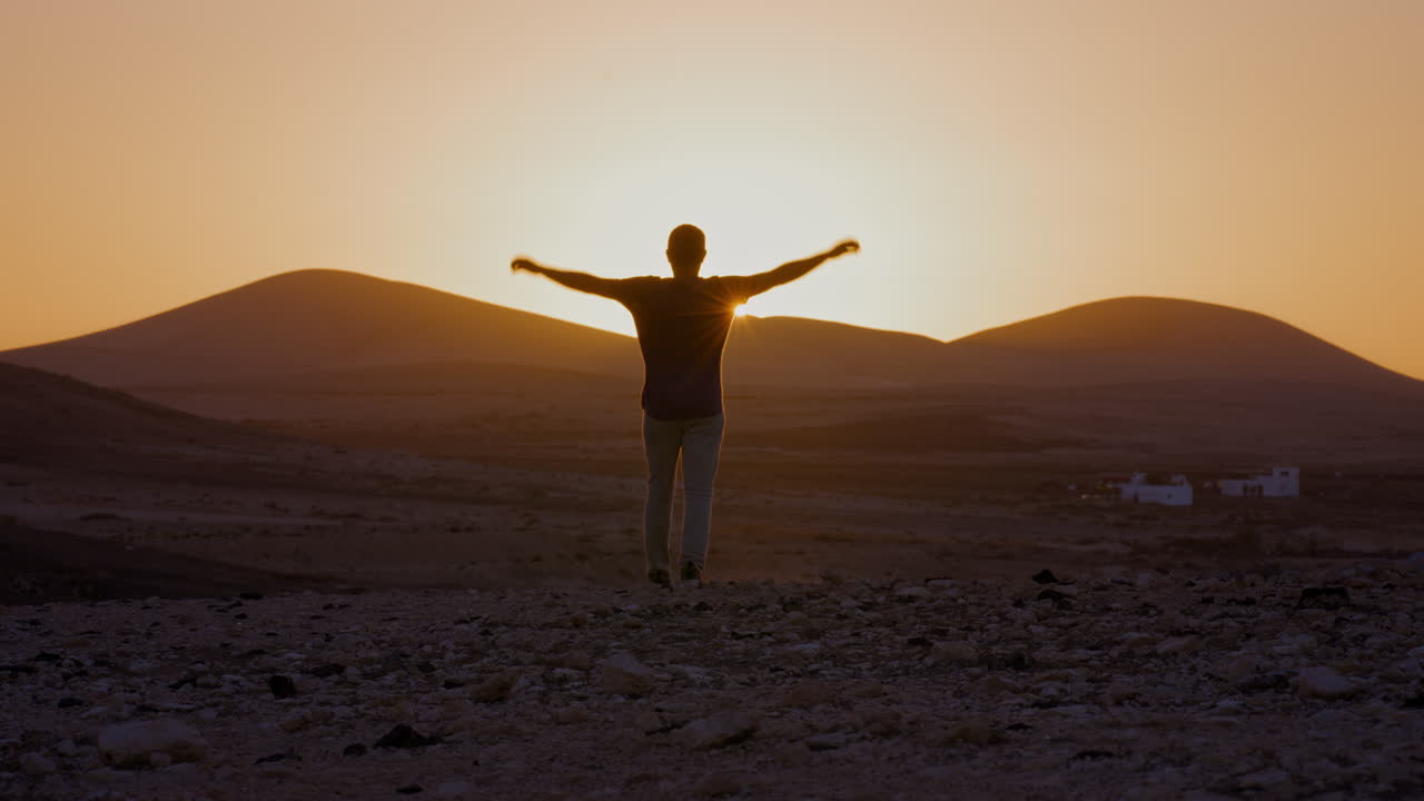 persona feliz levantando los brazos y caminando hacia la puesta de sol en la hora dorada con la cordillera en la parte de atrás