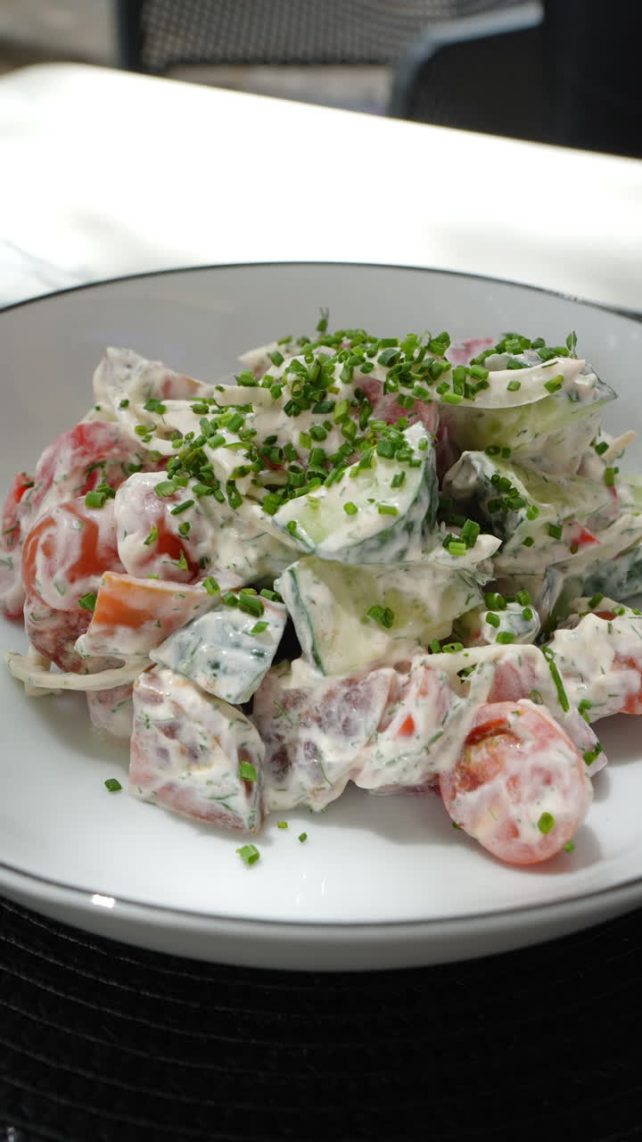 Vertical footage Gourmet summer salad featuring fresh tomatoes, cucumbers, creamy chive sauce nestled on pristine white ceramic plate, ready for elegant dining experience