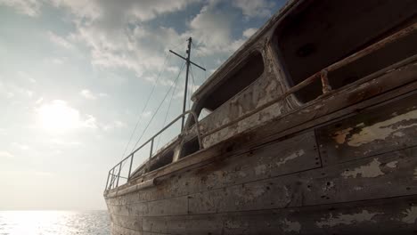 Cerca-De-Un-Viejo-Naufragio-Abandonado,-Ruina-De-Barco-Mar-Tranquilo-En-La-Parte-Trasera-Y-Cielo-Soleado,-Recuerdos-Del-Pasado