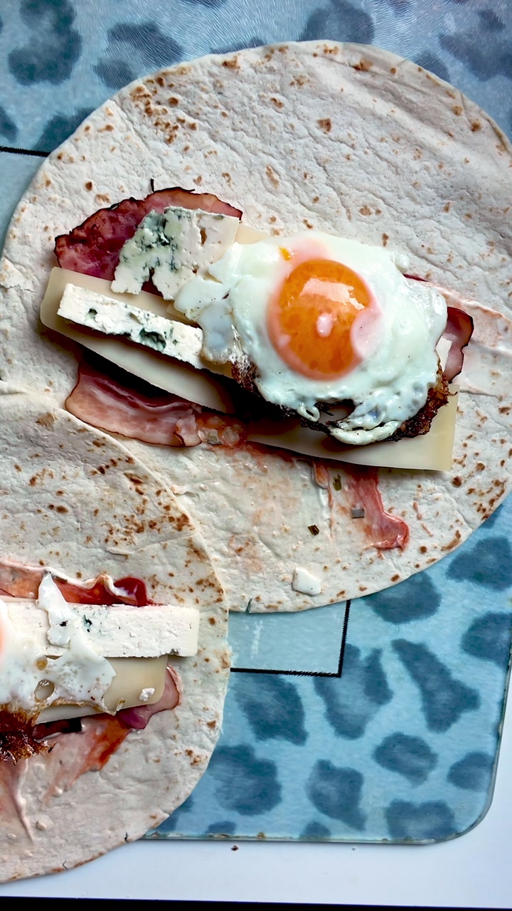 Making fried egg Tortilla wrap with cheese and meaty comfort food fillings
