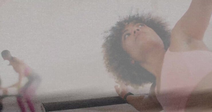 Low-angle filming woman holding barre stretching while second entering squatting for barre class